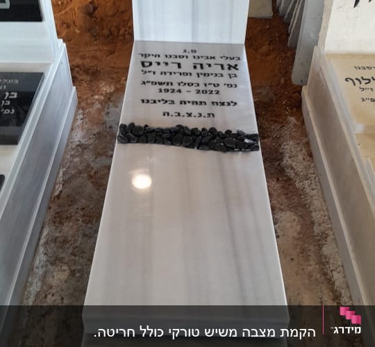 מצבה לבנה עם כיתוב בעברית ואבנים שחורות